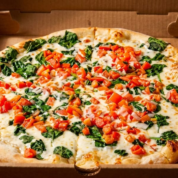 A freshly baked pizza with white cheese, spinach, and diced tomatoes in a cardboard box.
