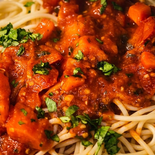 Close-up of spaghetti with chunky tomato sauce and fresh green herbs on a white plate.